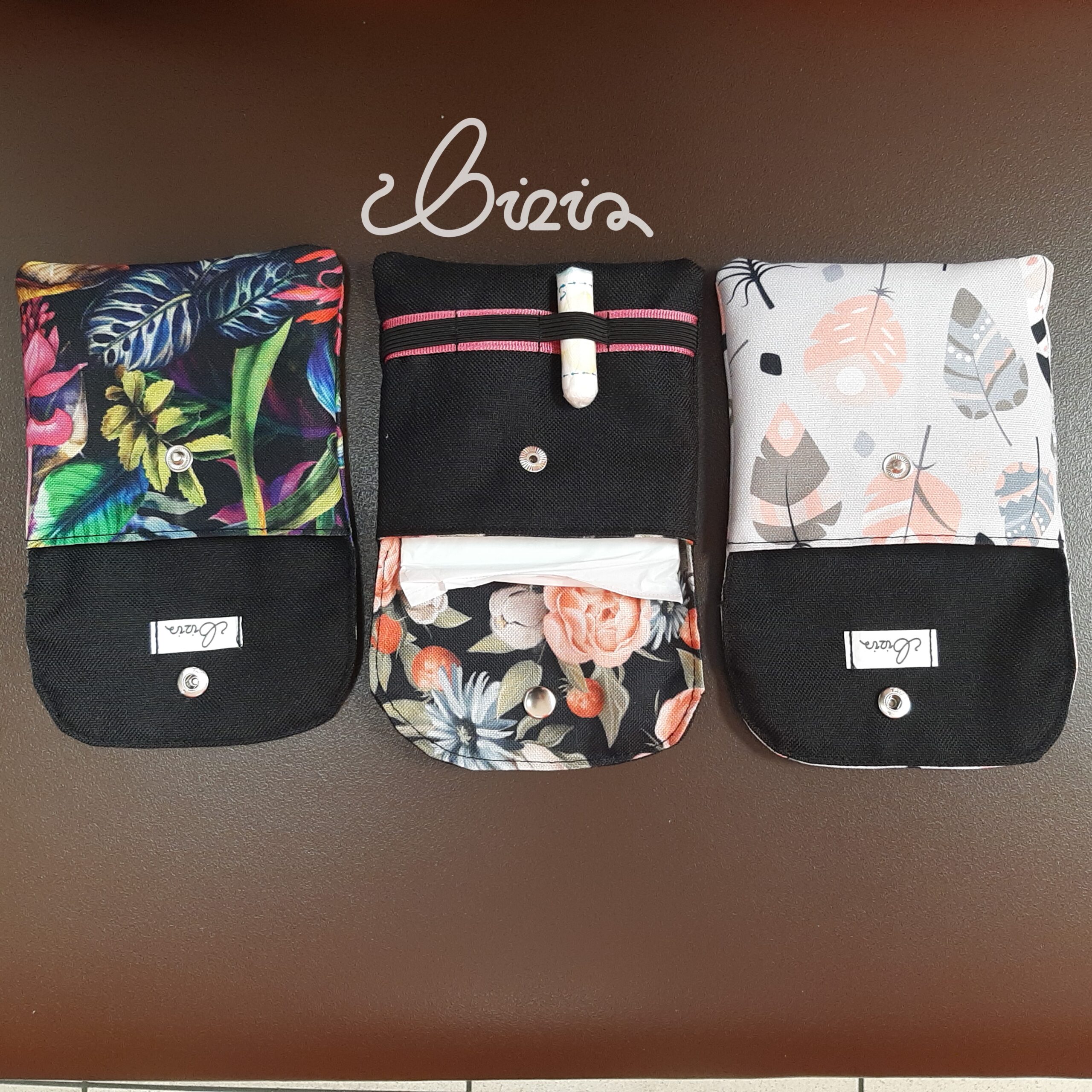 Etui na podpaski i tampony. Wykonane z materiału wodoodpornego. Wzór z piórami, różami i kwiatowy. Etui otwarte, wywrócone.