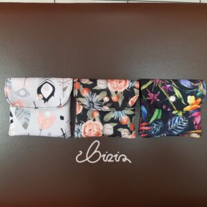 Etui na podpaski i tampony. Wykonane z materiału wodoodpornego. Wzór z piórami, różami i kwiatowy. Etui zamknięte.