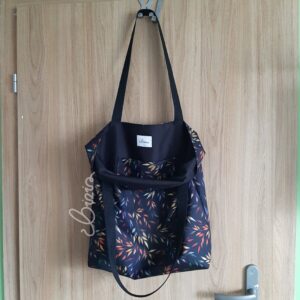 Torba na ramię we wzór jesiennych liści. Torba otwarta widać kolor podszewki. Torba na ramię na tle drewna.