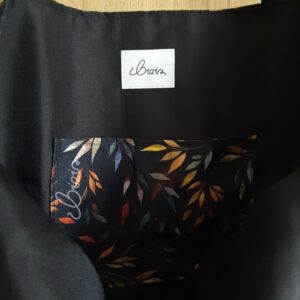 Torba na ramię we wzór jesiennych liści. Torba otwarta widać kolor podszewki. Na zdjęciu można zobaczyć kolor kieszeni. Torba na ramię na tle drewna.